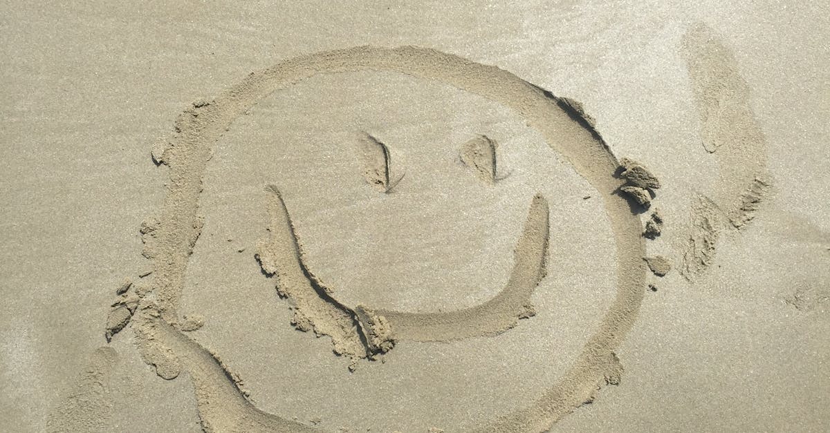 A smiley face drawn in sand on a sunny beach, captured with shoes visible.